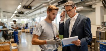 Mid adult engineer and young worker cooperating while analyzing reports in steel factory.